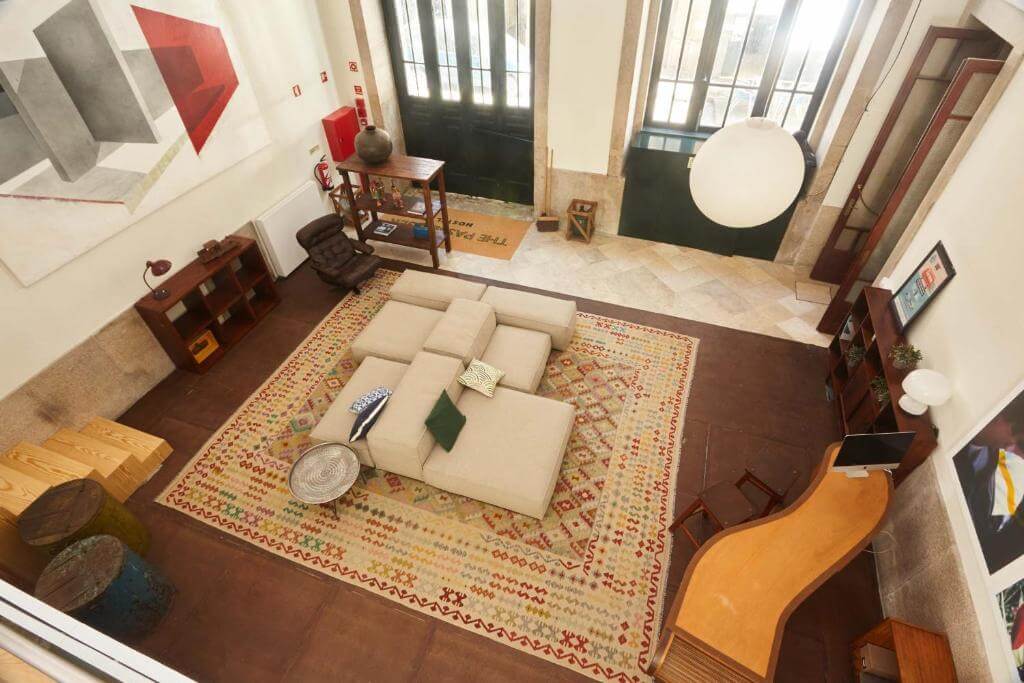 The Passenger Hostel 挑高交誼大廳，中央沙發、地毯與整面高窗