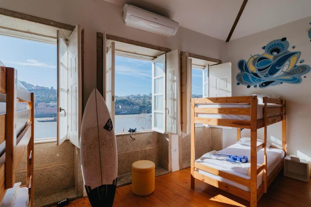 Happy Porto Hostel 女生房，木頭上下舖與面河的整排落地窗，牆上有藍色浪花彩繪