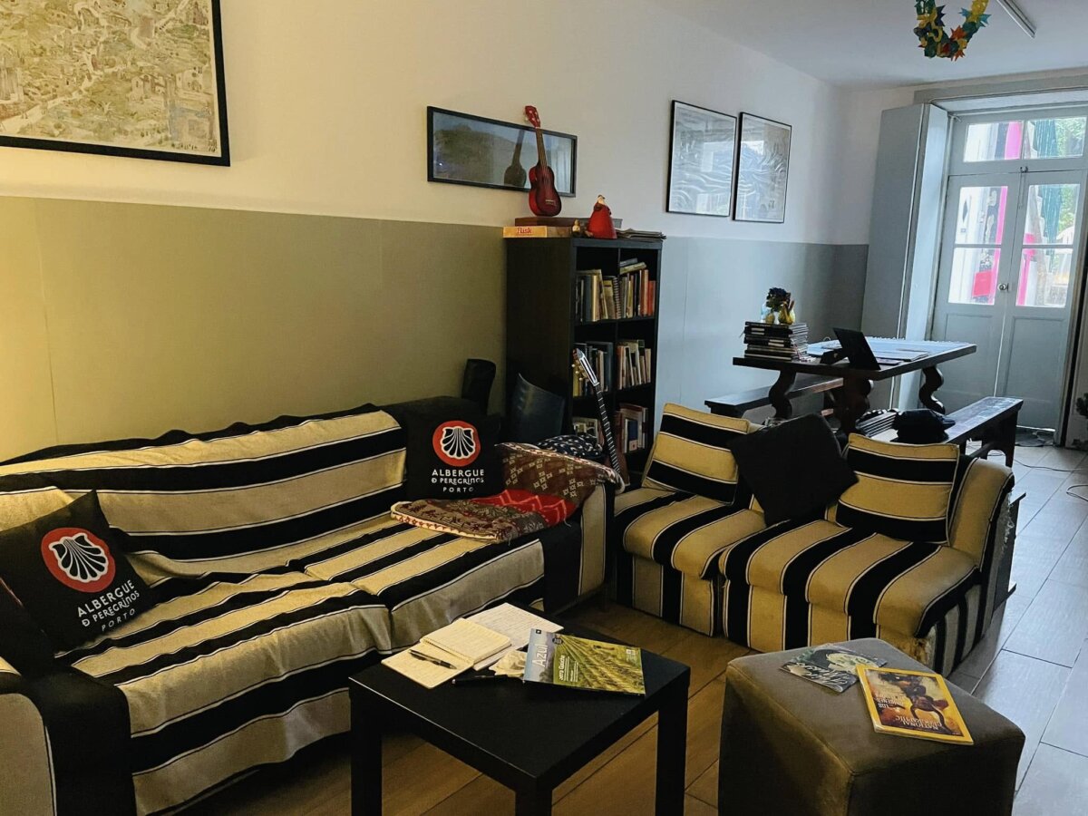 Albergue de Peregrinos do Porto 的交誼小客廳,條紋沙發、書架與扇貝抱枕