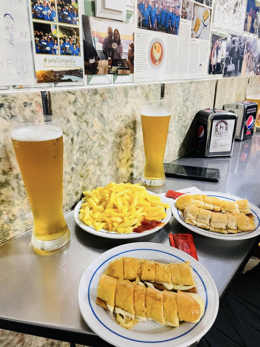GAZELA 桌上切成段的葡萄牙熱狗、薯條與兩杯啤酒，牆上貼滿客人照片