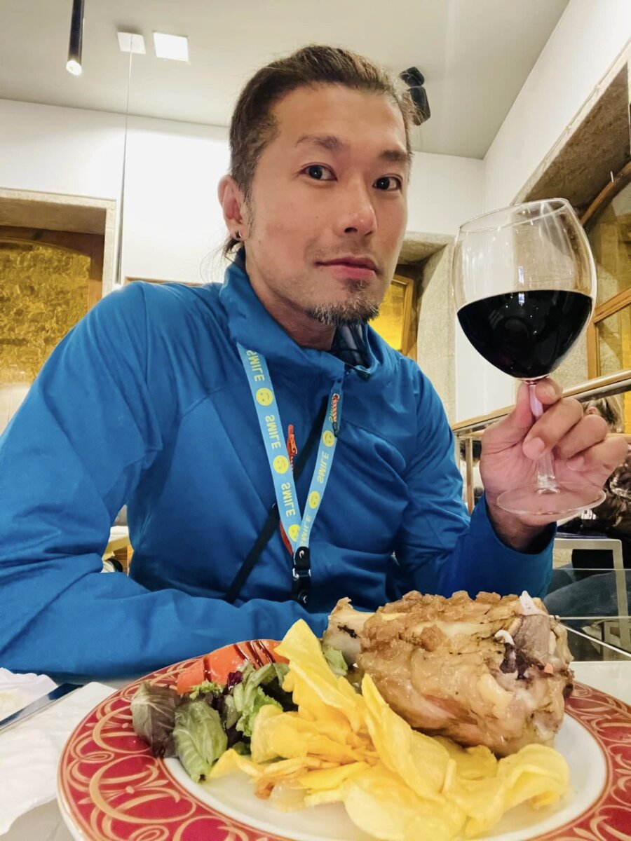 駐站朝聖者史坦力在 Casa Manolo 舉起紅酒杯，桌上是豬大骨肉配薯片與生菜