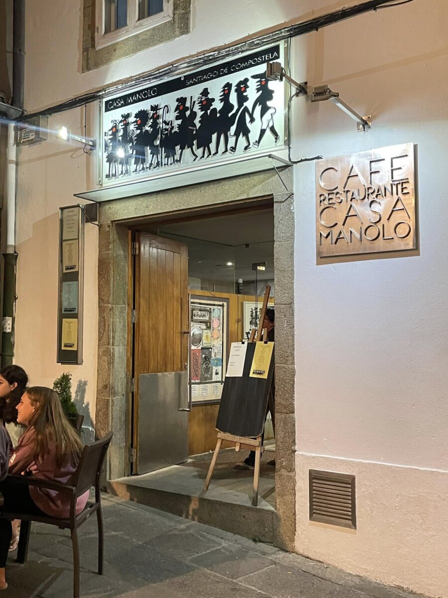 Casa Manolo 店門口夜景，招牌上是朝聖者剪影，牆上掛著 Cafe Restaurante Casa Manolo 銅牌