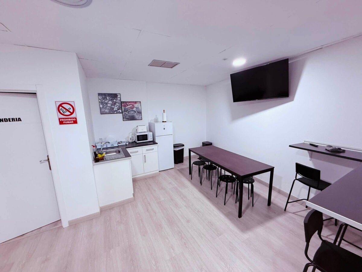 O Albergue de Fene 的公共空間，左邊是有微波爐和冰箱的小廚房，中間長桌，牆上掛電視