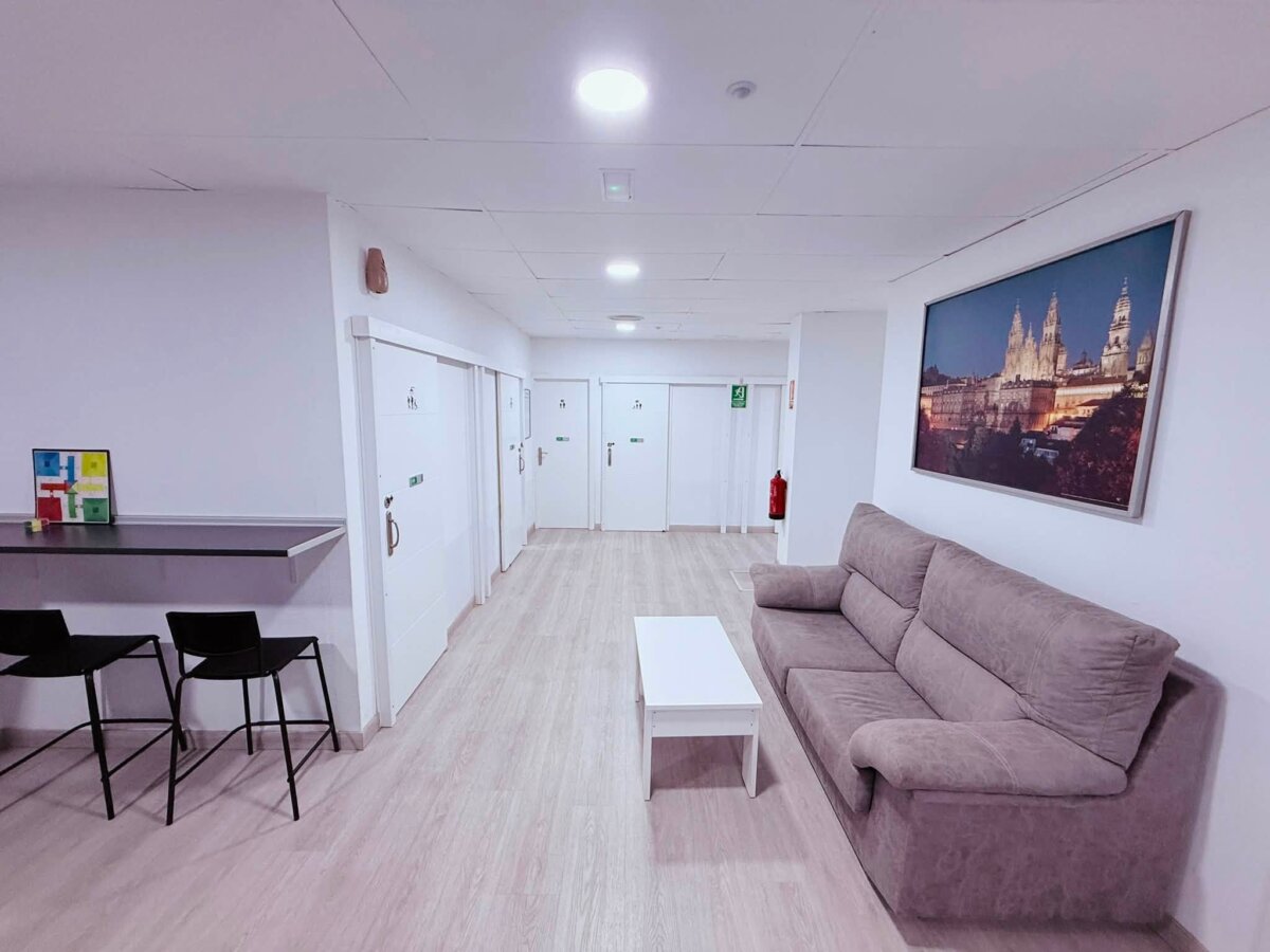 O Albergue de Fene 的走廊休息區，灰色沙發和白色小茶几，牆上掛聖地亞哥大教堂夜景畫