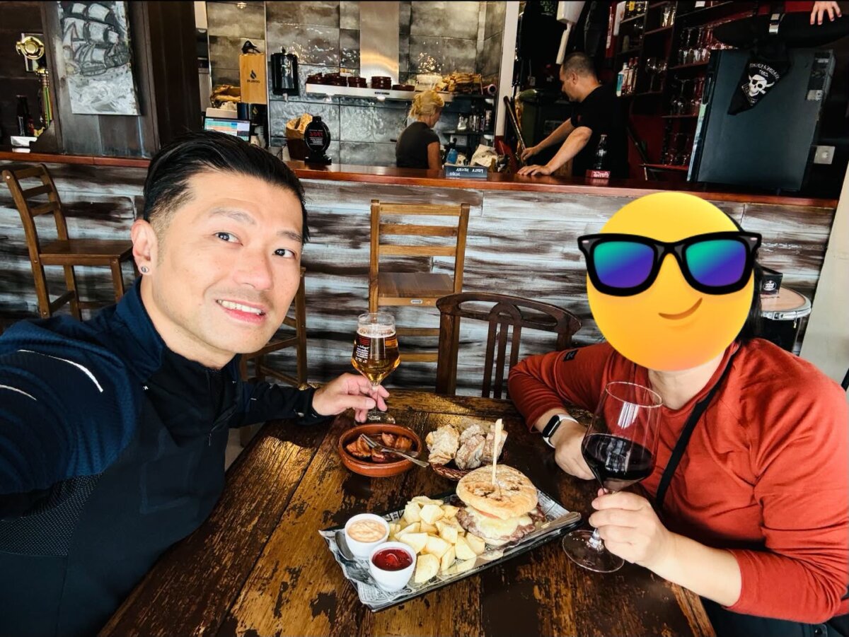 Miño 小酒館的午餐，木桌上一盤圓麵包歐式漢堡配馬鈴薯和兩種沾醬，史坦力舉著啤酒，背景是掛著海盜旗的吧台